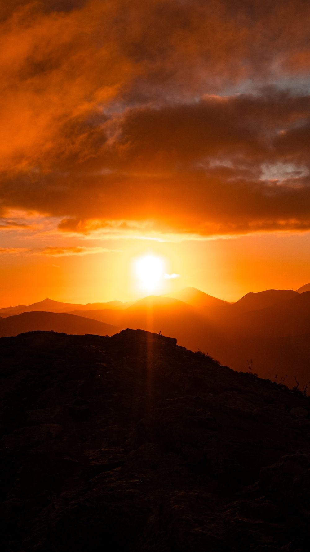 The sun setting in an orange sky behind layered hill silhouettes
