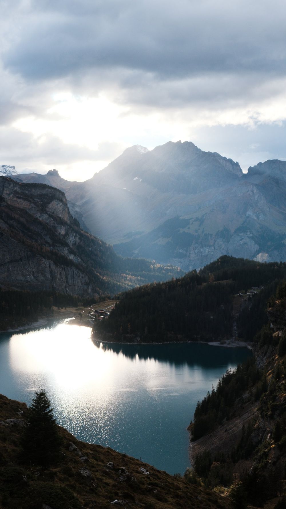 Beams of sunlight breaking through clouds over a mountain valley and a dark blue lake