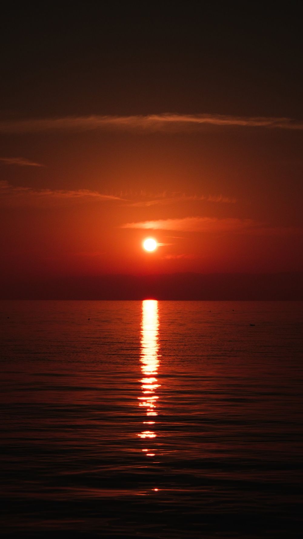 Deep red sunset over a calm sea with a bright reflection of the sun on the water