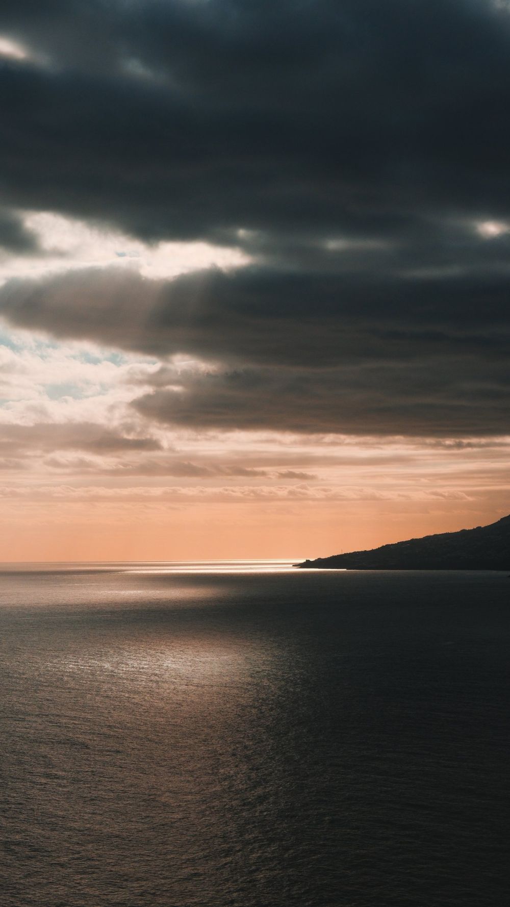 Dark storm clouds opening to an orange glow over a calm sea and a distant headland